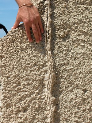 Photograph of a vertical quarry wall showing a single deformation band (rib-like feature in a vertical orientation) which is overprinted by pressure solution seams (two lineaments with negative relief) in carbonate grainstone, Calla Rossa area, Favignana Island, Sicily, Italy.