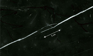 Calcite veins (white) in a cut and polished surface of a tile of black marble building stone from Italy. The thicknesses of the veins vary from hairline to about 3.5 mm. Two segments of the veins overlap for about 5 cm, which, together with large thickness variation, reveals multi-stage opening history. Sample courtesy of Isik Aydinli.
